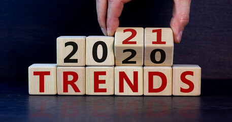 Business concept of planning 2021. Male hand flips wooden cubes and changes the inscription 'Trends 2020' to 'Trends 2021'. Beautiful dark wooden background, copy space.