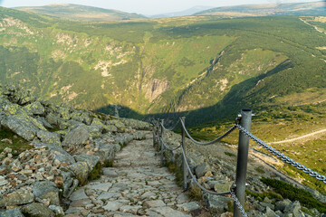 A steep mountain trail with handrails on chains, bright mountains in the background.