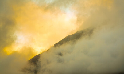 Sunlight breaking through dense storm clouds over a mountain ridge.