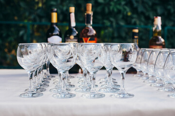 glass goblets stand in rows next to alcohol bottles