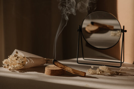  palo santo with jet of smoke, mirror and dried flowers on a neutral background. Abstract trendy picture. Minimalistic wabi sabi style.