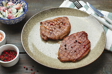 Two grilled ribeye steaks, spices and tomato-cucumber salad with sour cream