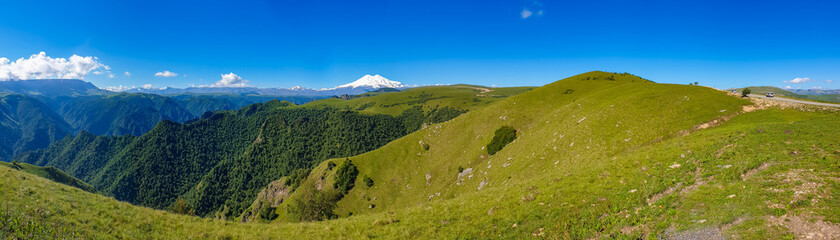 Amazing panorama of caucasian mountain, volcano Elbrus with green fields, blue sky background. Elbrus panorama landscape view