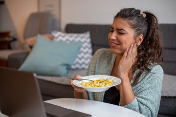 A smiling young woman is eating pasta and having a toothache in the livingroom.