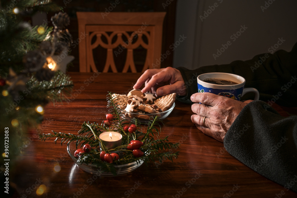 Wall mural hands of an elderly single man sitting alone at a table with christmas cookies, coffee and festive d