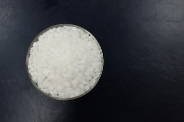 Top view of sodium or potassium hydroxide white chemical compound pellets or prills in a petri dish in black background.