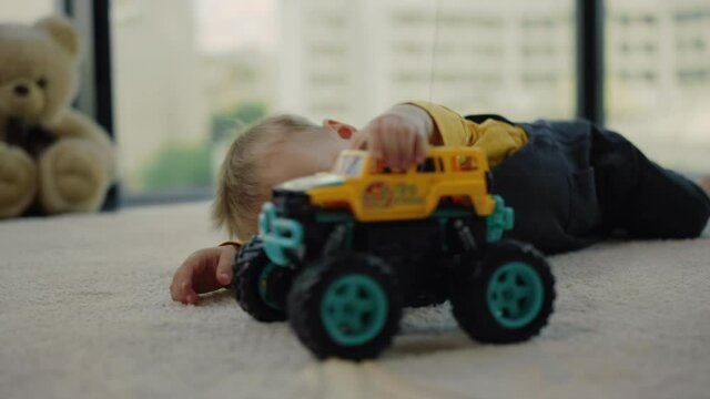 Cheerful boy lying on rug with toy truck. Baby playing with toy car at home.