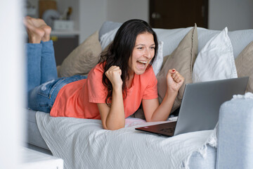 The girl lies on the couch, rejoicing, clenching her hands into fists. The emotion is success, victory, achievement