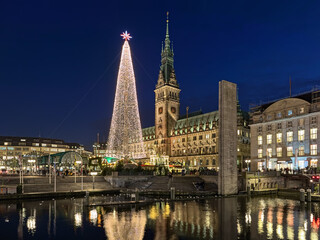 Hamburg, Germany. Christmas market with large illuminated Christmas tree at Town Hall square in front of Hamburg Town Hall in dusk. View from Alsterarkaden at Kleine Alster river.