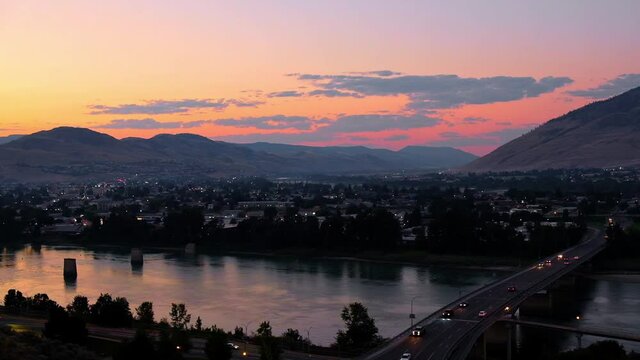 Stadt an Fluss bei Sonnenuntergang. Autos fahren &uuml;ber Br&uuml;cke.