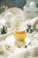 Details of still life in the home interior living room. Orange Opened plastic container, jar.of cream over Christmas lights bokeh in home. holiday decoration, magic Christmas. Selected focus