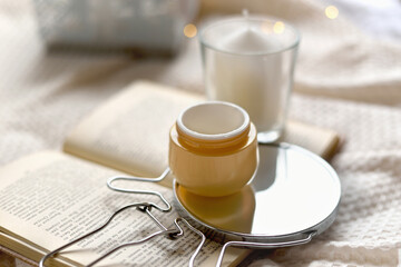 Details of still life in the home interior living room. Orange Opened plastic container, jar.of cream over Christmas lights bokeh in home. Winter mood, holiday decoration, magic Christmas. 