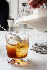 White Russian cocktail preparation. Pouring cream into the glass