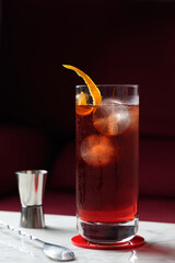 Americano Cocktail with Orange Twist on a marble table. Red sofa as a background. Front view
