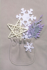 Happy New Year composition in the pocket of a gray fleece jacket. Christmas or winter still life made of snowflakes, handmade star and cypress branch on gray background. Flat lay, top view.