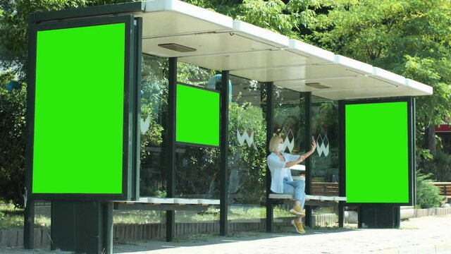 A bus stop in Istanbul, a vertical billboard ad at the bus stop. Green box for placing on advertising posters.A woman in a medical mask takes a selfie.