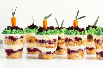 Macro shot of the trifle with carrot shaped marzipan and grass decoration on top. Layered dessert in a glass on the white background.