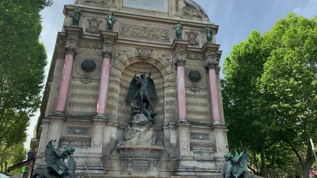 Footage of historical fountain called "La Fontaine Saint Michel" with sculpted dragons in Paris. It is a sunny summer day. Camera moves forward.