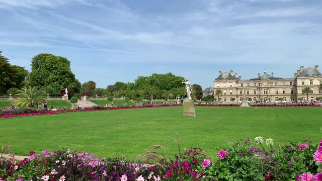 Footage of people walking and relaxing at famous garden called "Jardin Du Luxembourg" and palace in Paris. It is a sunny summer day. Camera pans right.