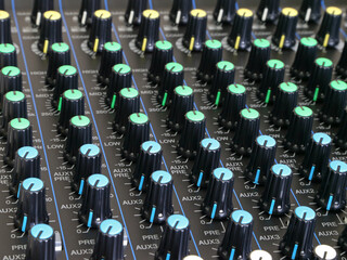 The control knobs of a professional audio mixing board console are shown in a closeup view.