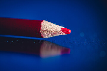 Closeup of a red colored pencil on a reflective surface