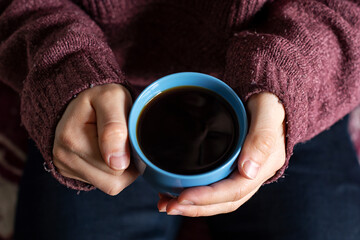 Close up from above angle of a blue cup of coffee holded by a person hands
