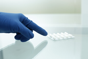 A hand in a blue medical glove points to a package of white pills
