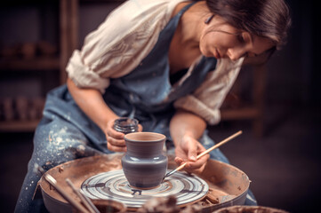 Beautiful potter female student creates a new pottery from clay on a potter's wheel. Handcraft.