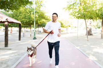 Naklejka na ściany i meble Man in his 30s running with a husky dog