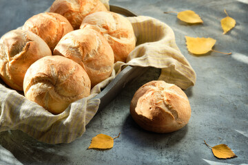Kaiser, or Vienna buns in bread basket on dark rustic background with yellow Autumn leaves.