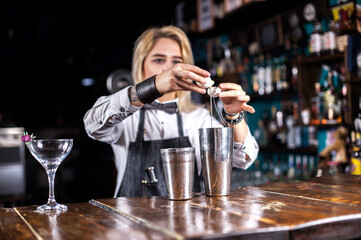 Girl barman mixes a cocktail behind the bar