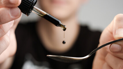 Consuming cbd oil for health improvement. Extract of cannabis hemp plants dropping on spoon.