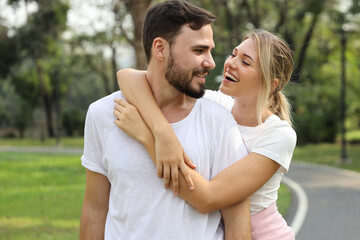 Fototapeta premium Young caucasian girl wearing white T-shirt standing and hugging her boyfriend with happy smiling face in park outdoor during summer season. (healthy or friendship concept)