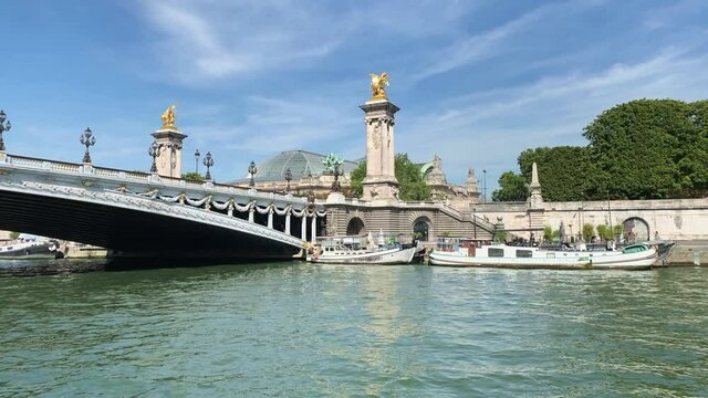 Footage of moored boats by Seine river, bridge called "Pont Alexandre III" and Grand Palace in Paris. It is a sunny summer day. Camera moves forward.