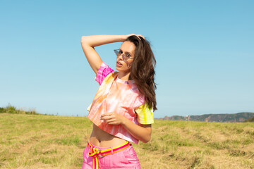 Model with long hair and glasses wearing a pink t-shirt above the navel with a defiant posture...