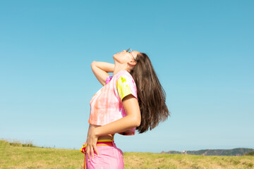 Model dressed in pink with long hair throwing her head back in a casual pose with a blue sky in the background on a sunny summer day