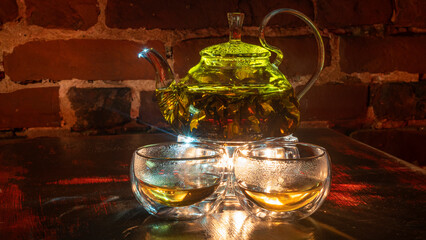 Boiling water and willow-herb or tea in a glass teapot. Two glass teacups. Red brick background. Vintage.