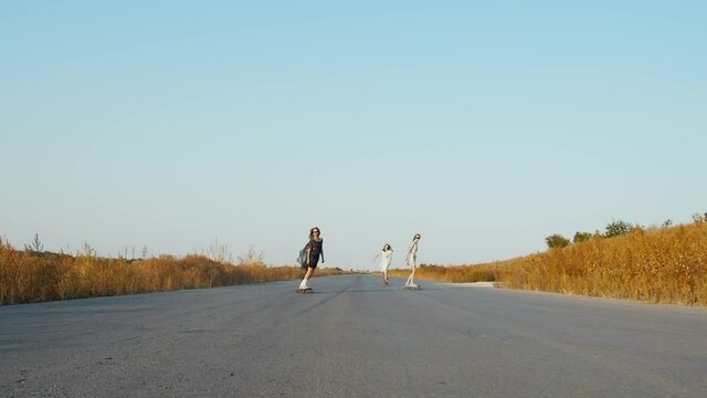 Women in sundresses are longboarding on the road, sunset, 4k
