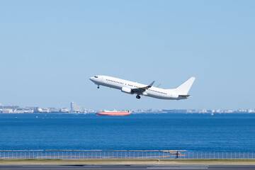 羽田空港を離陸する飛行機、青空を背景に東京湾を航行する船