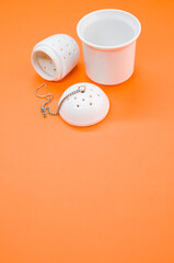 Vertical shot of a white tea strainer and an infuser isolated on an orange background