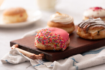 Close up of a donut with sprinkles and pink icing on a board with a glass of milk. Ideal for recipe page or magazine editorial