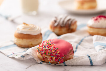 A donut with sprinkles and pink icing in front of a group of mixed donuts and a glass of milk. Ideal for recipe page or magazine editorial
