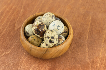 Fototapeta premium fresh quail eggs speckled white and dark in a wooden bowl on a wooden background