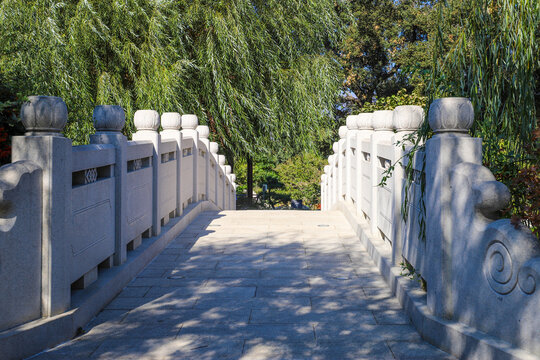 A Stone Bridge To Nowhere In The Japanese Garden Surrounded By Lush Green Trees And Weeping Willow Trees  At Huntington Library And Botanical Gardens In San Marino, California