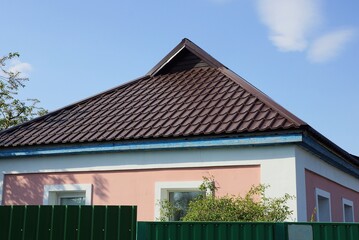 brown tiled roof on a rural house behind a green metal fence against a blue sky on a sunny day