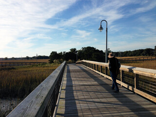 A man walking along the boardwalk over the salt marsh at Shem Creek, near Charleston, South Carolina, USA.