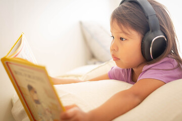 Little girl reading a book and listening to music and audio books at home.