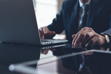 Businessman in black suit working on laptop computer and digital tablet in office