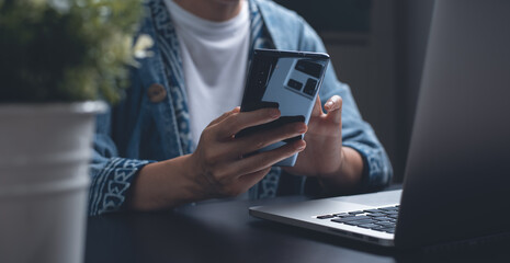 Business woman using mobile smart phone during online working on laptop computer at night from home office