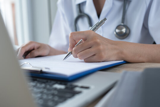 Female doctor filling medical document, health report or prescription on clipboard in medical office